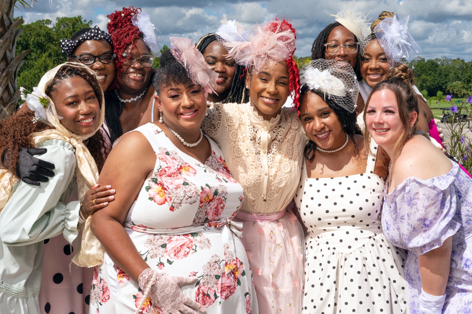 The 2026 Bride Tribe gathered close together at brunch in garden-party dresses, pearls and headpieces, all smiling