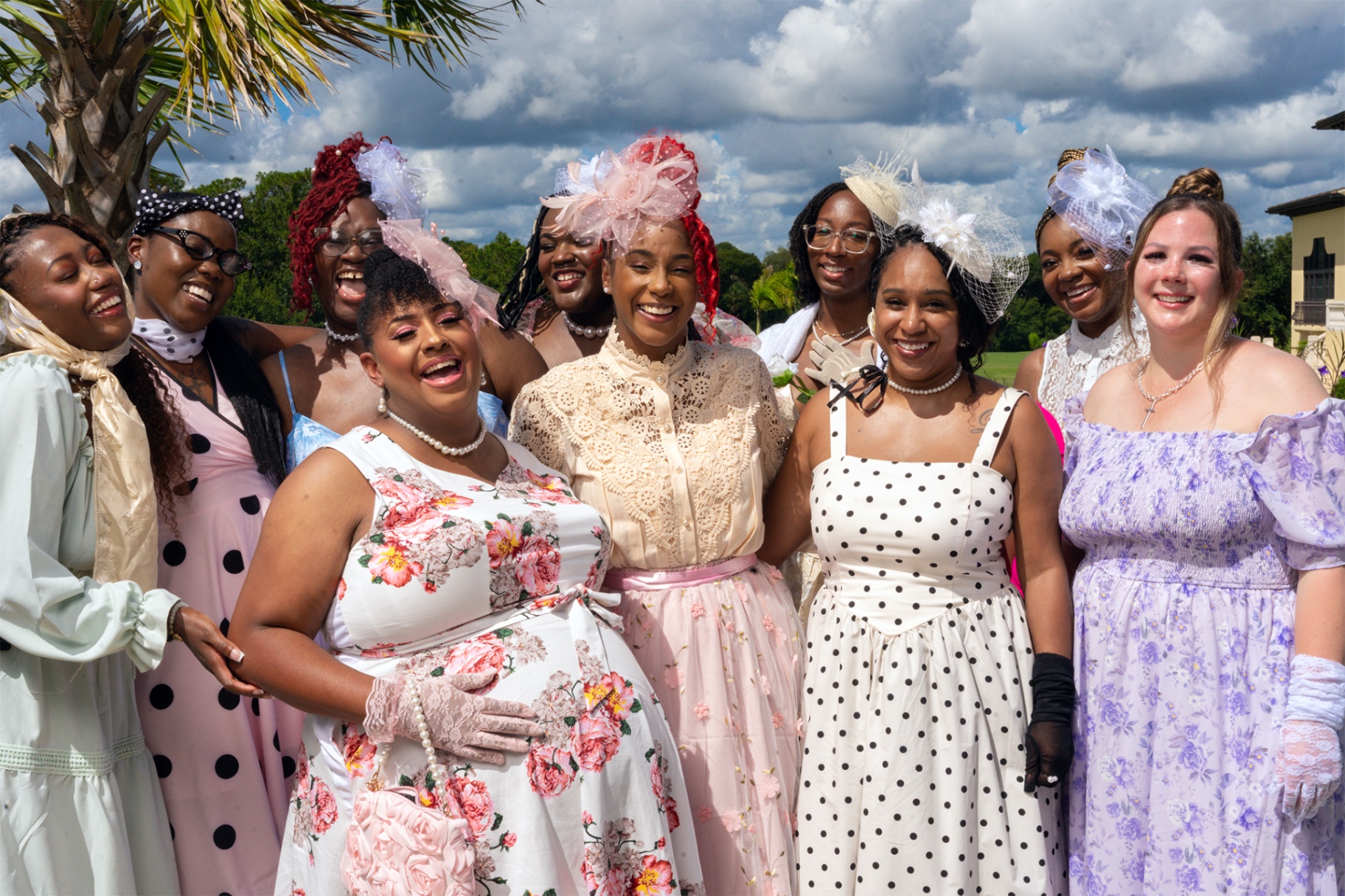 The 2026 Bride Tribe gathered outdoors in garden-party dresses, pearls and headpieces, all laughing together